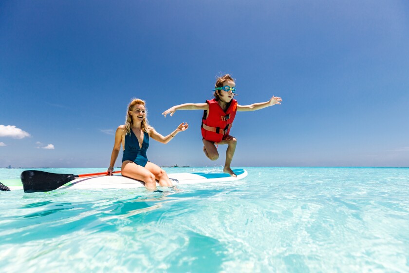 Happy single mother and son having fun on paddle board at sea.